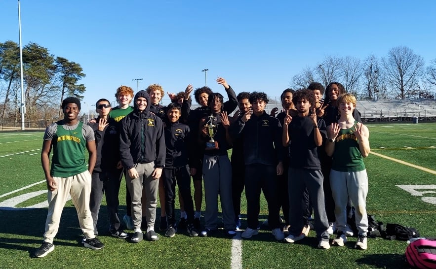 A group of high school athletes proudly poses on a football field, holding a trophy and celebrating a victory.