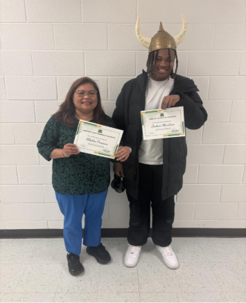 Ms. Vasquez and Joshua Hawkins proudly holding student and staff member of the month certificates, with one wearing a playful Viking helmet.