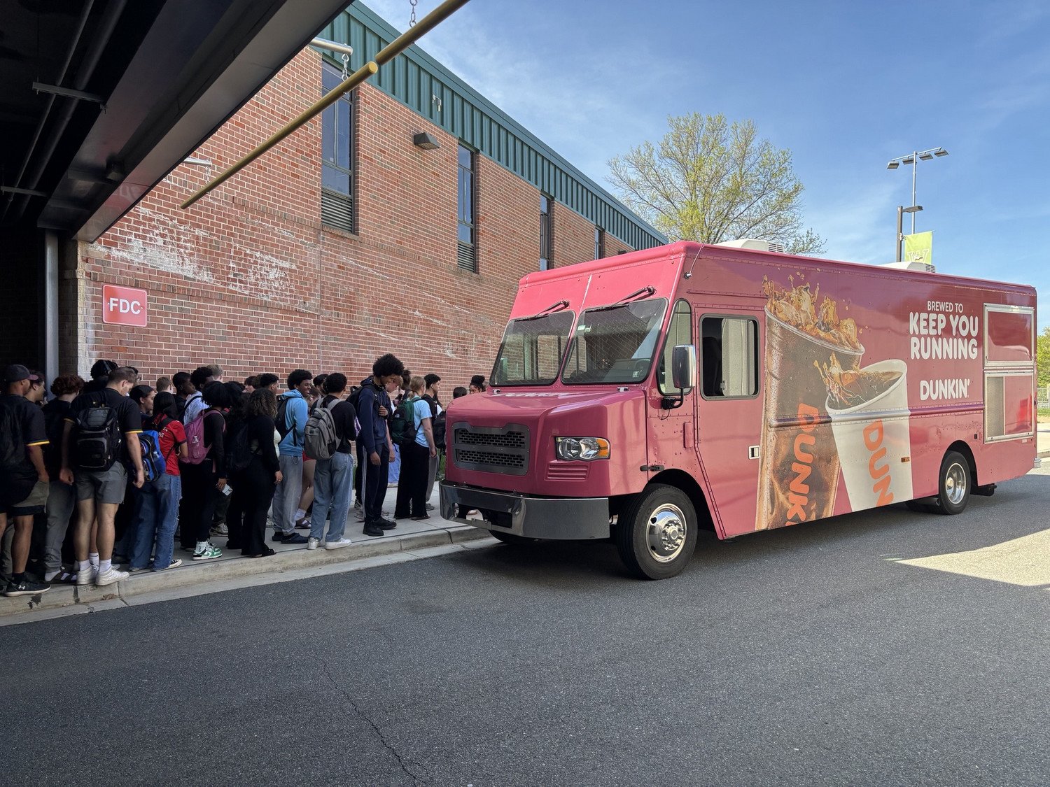 Dunkin' food truck parked beside a line of students waiting to be served.