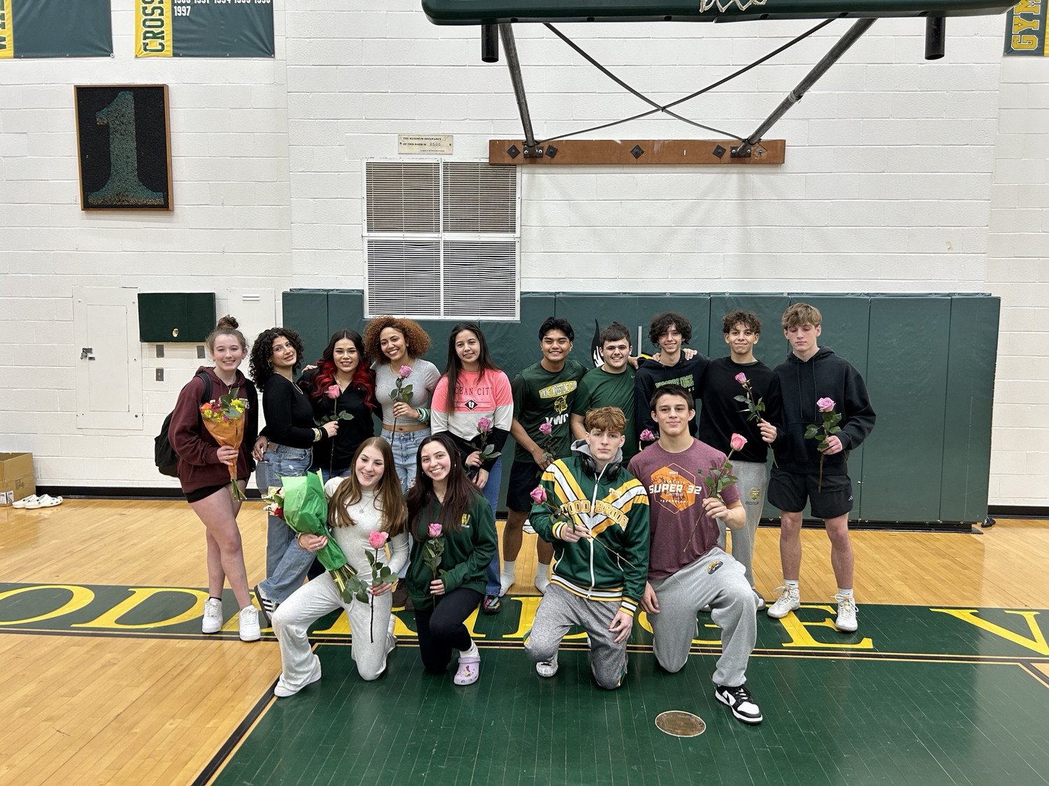 WSHS senior wrestlers, some holding roses, pose together in a gymnasium, celebrating senior night.
