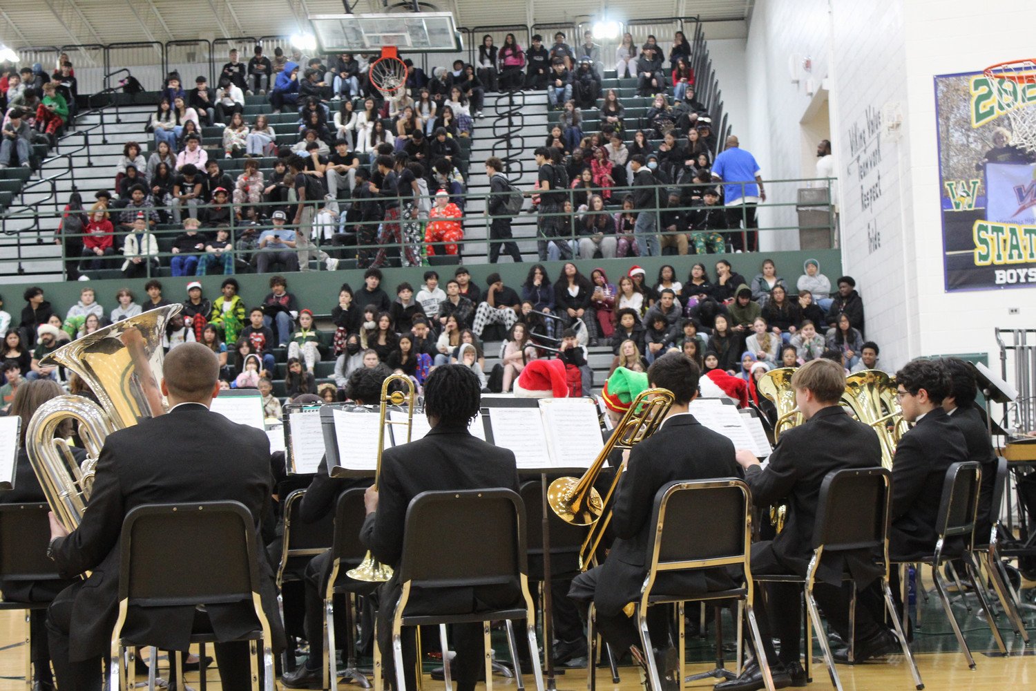 A school band performs in front of a packed audience in a gymnasium, showcasing a variety of brass instruments.
