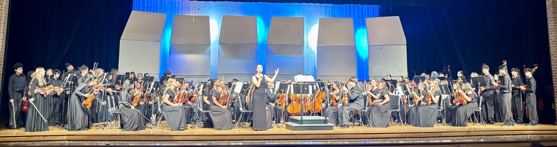 Woodbridge Senior high School's orchestra performing on stage, featuring musicians in black attire with a conductor leading the ensemble.