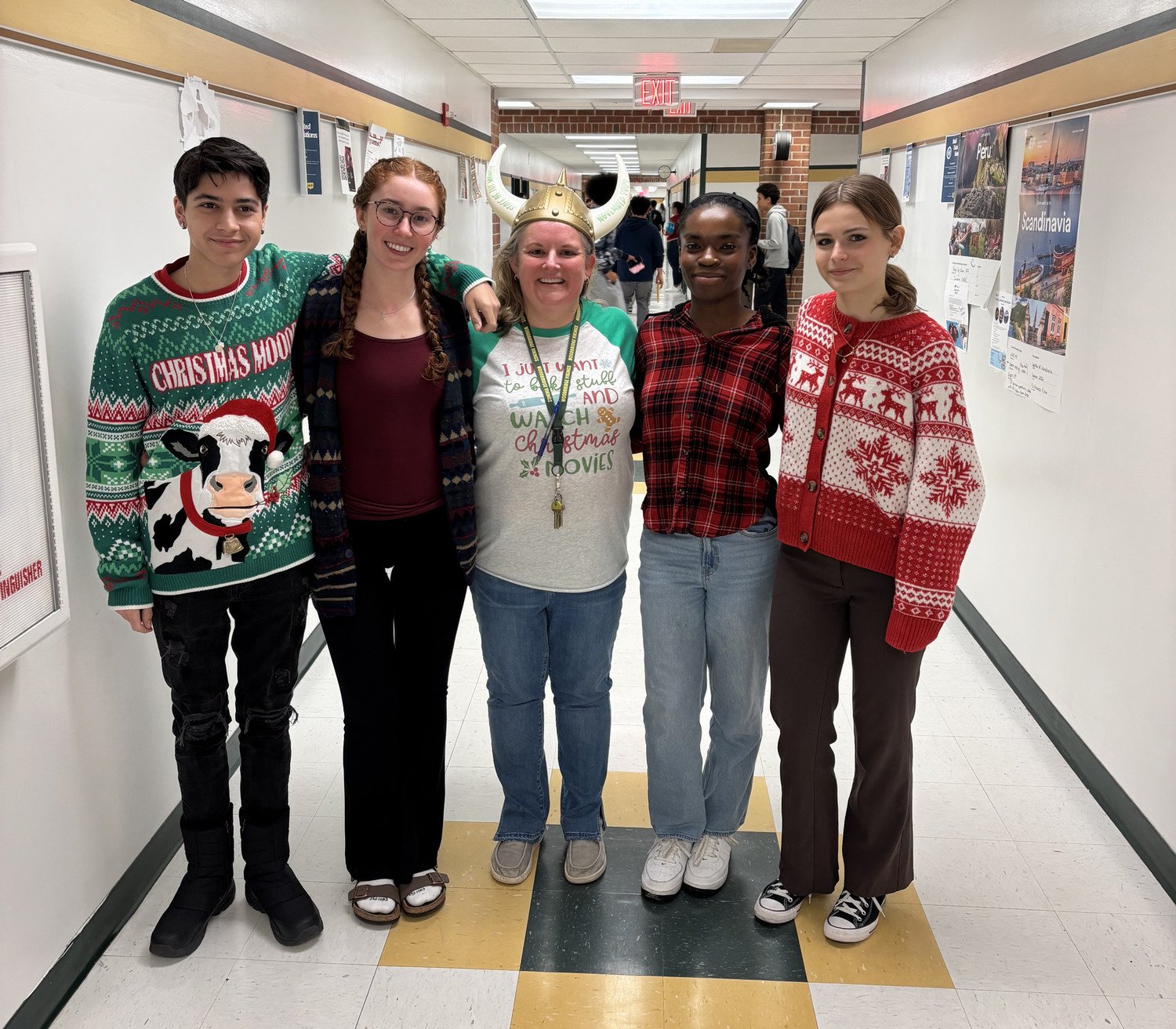 The Student Voices Committee and their sponsor standing together in a school hallway, dressed in festive holiday attire and sweaters.