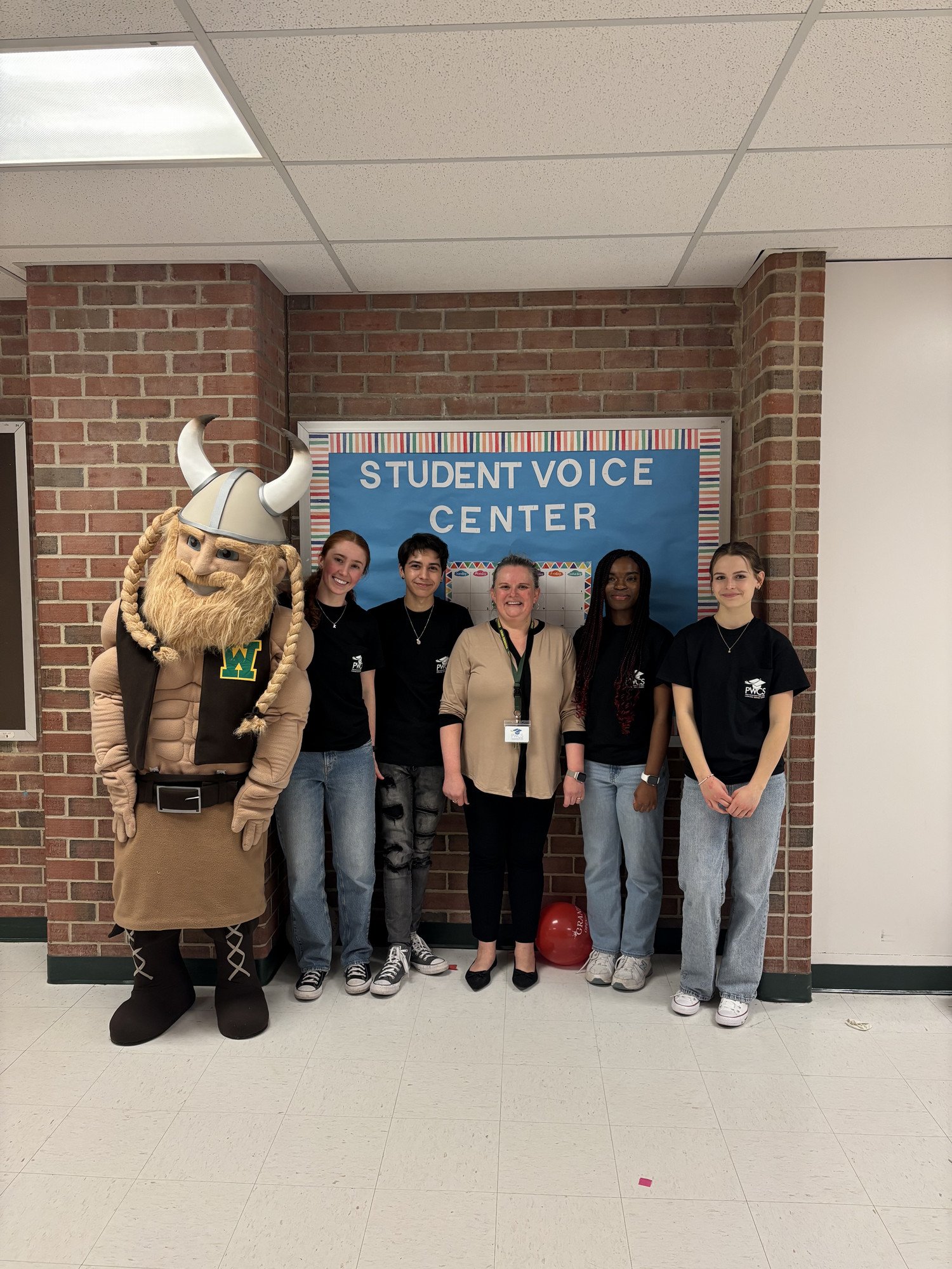 Group of five people, including a mascot in a Viking costume, posing in front of a "Student Voice Center" sign.