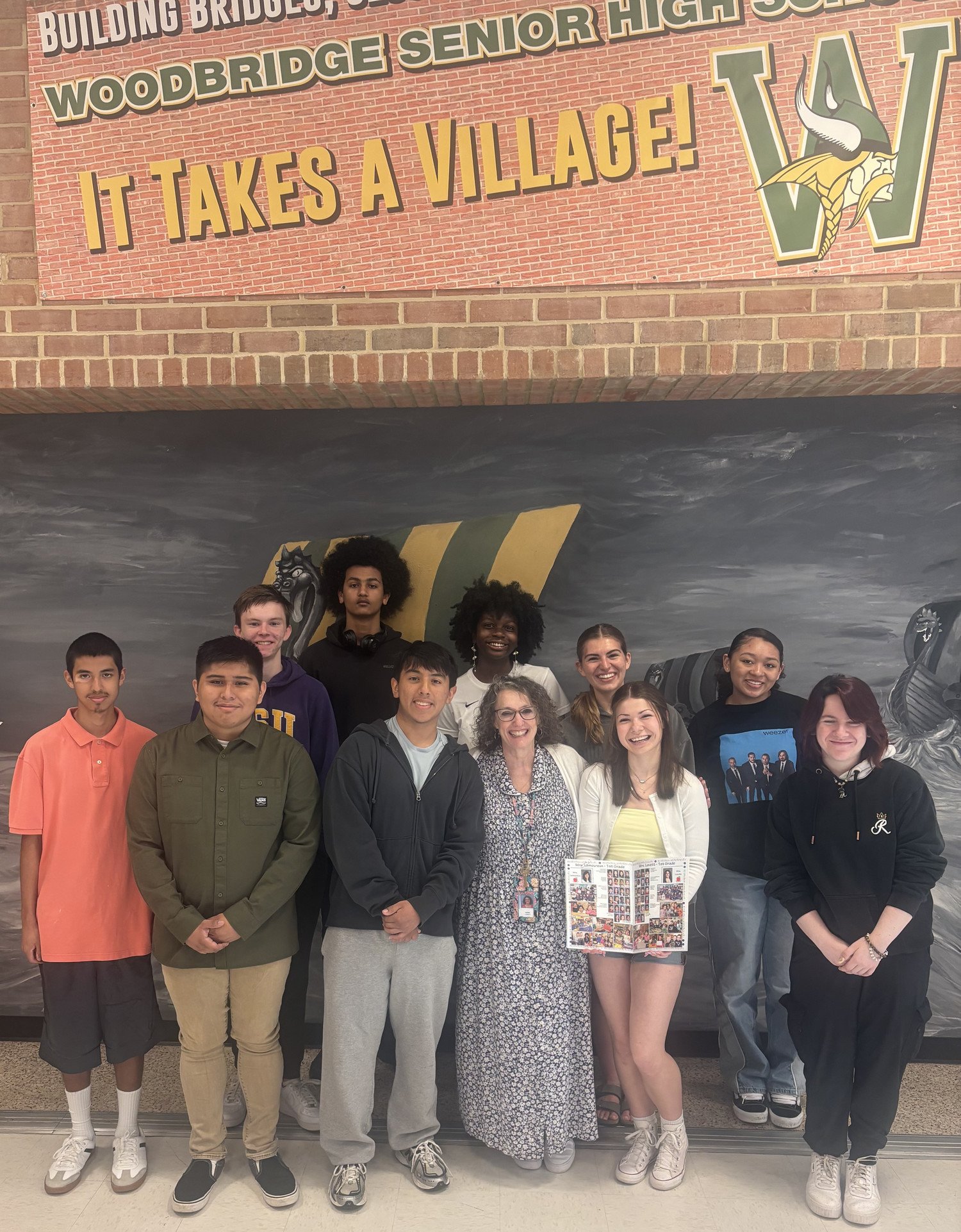 WSHS students with their former first grade teacher Ms. Lovett, standing together in front of a mural at Woodbridge Senior High School, celebrating community and teamwork.