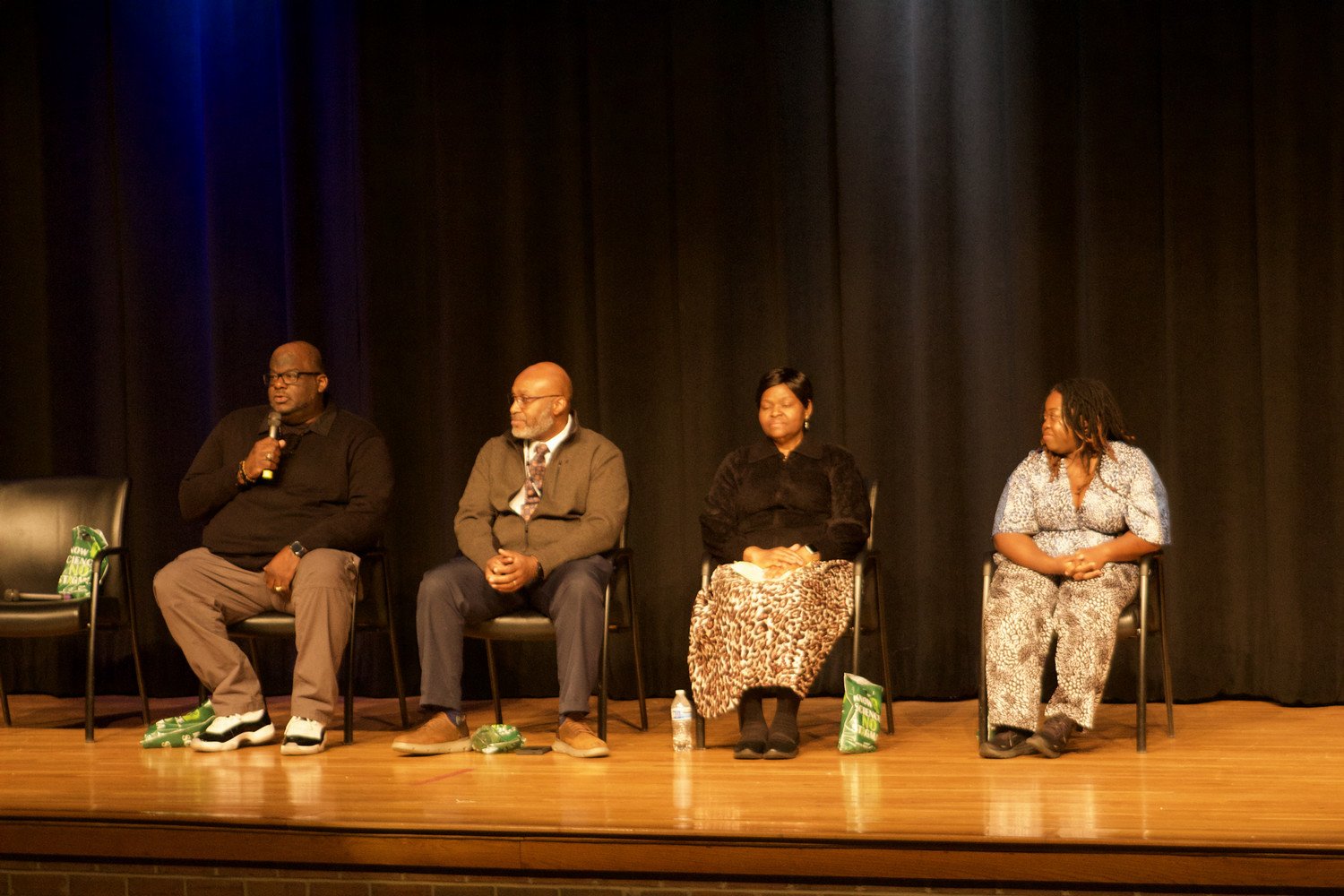 A panel discussion featuring four speakers, seated on stage, discussing a topic in front of an audience.