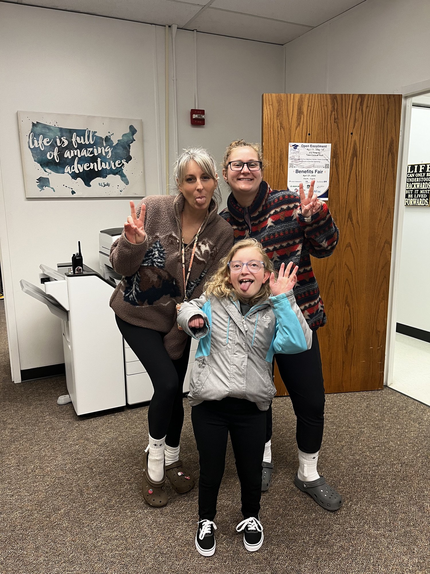 Administrative Assistants and student pose playfully, sticking out their tongues and making peace signs in a cheerful indoor setting.