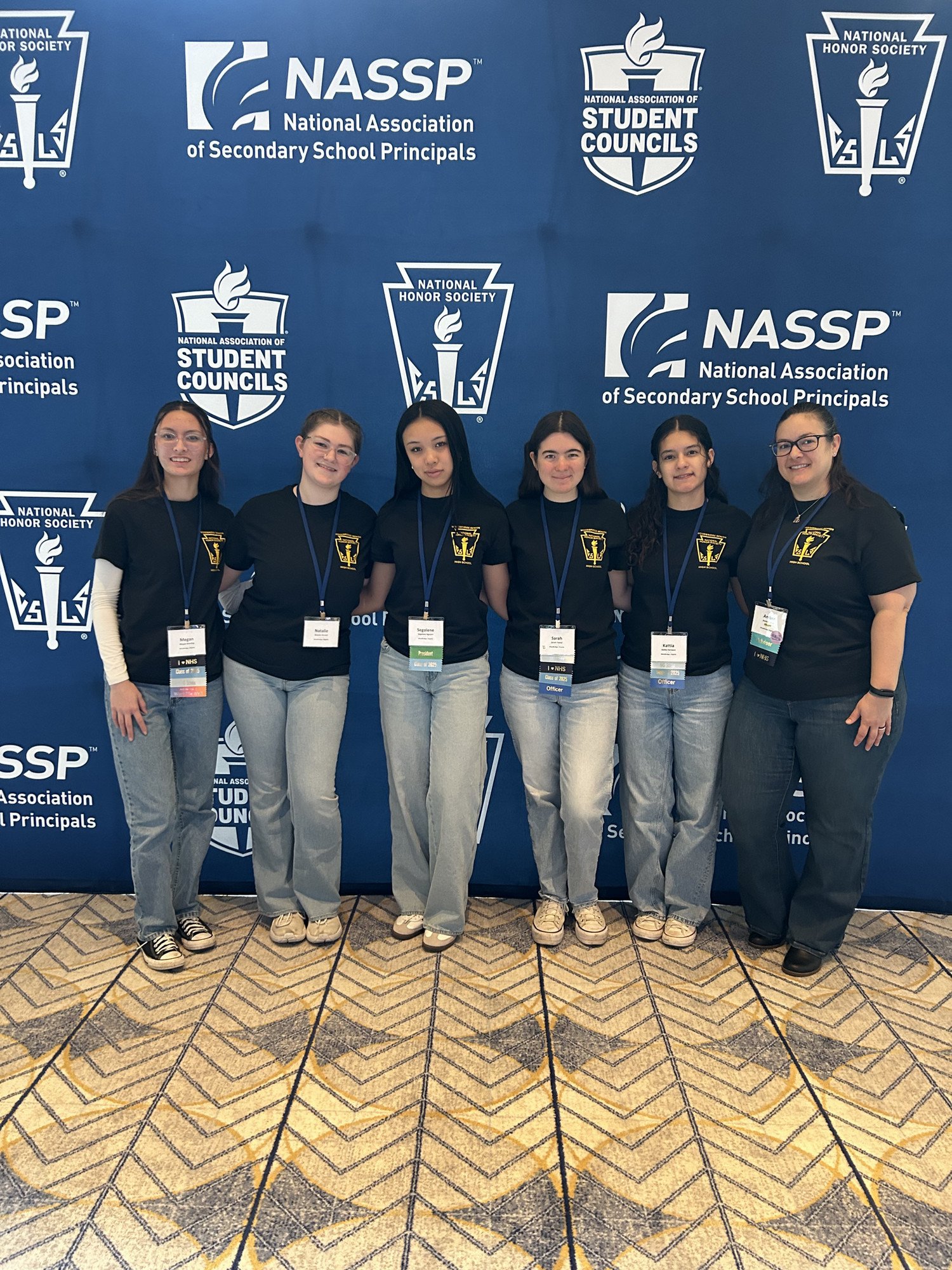 Group of six students wearing matching t-shirts posing in front of a conference backdrop featuring the NASSP logo.