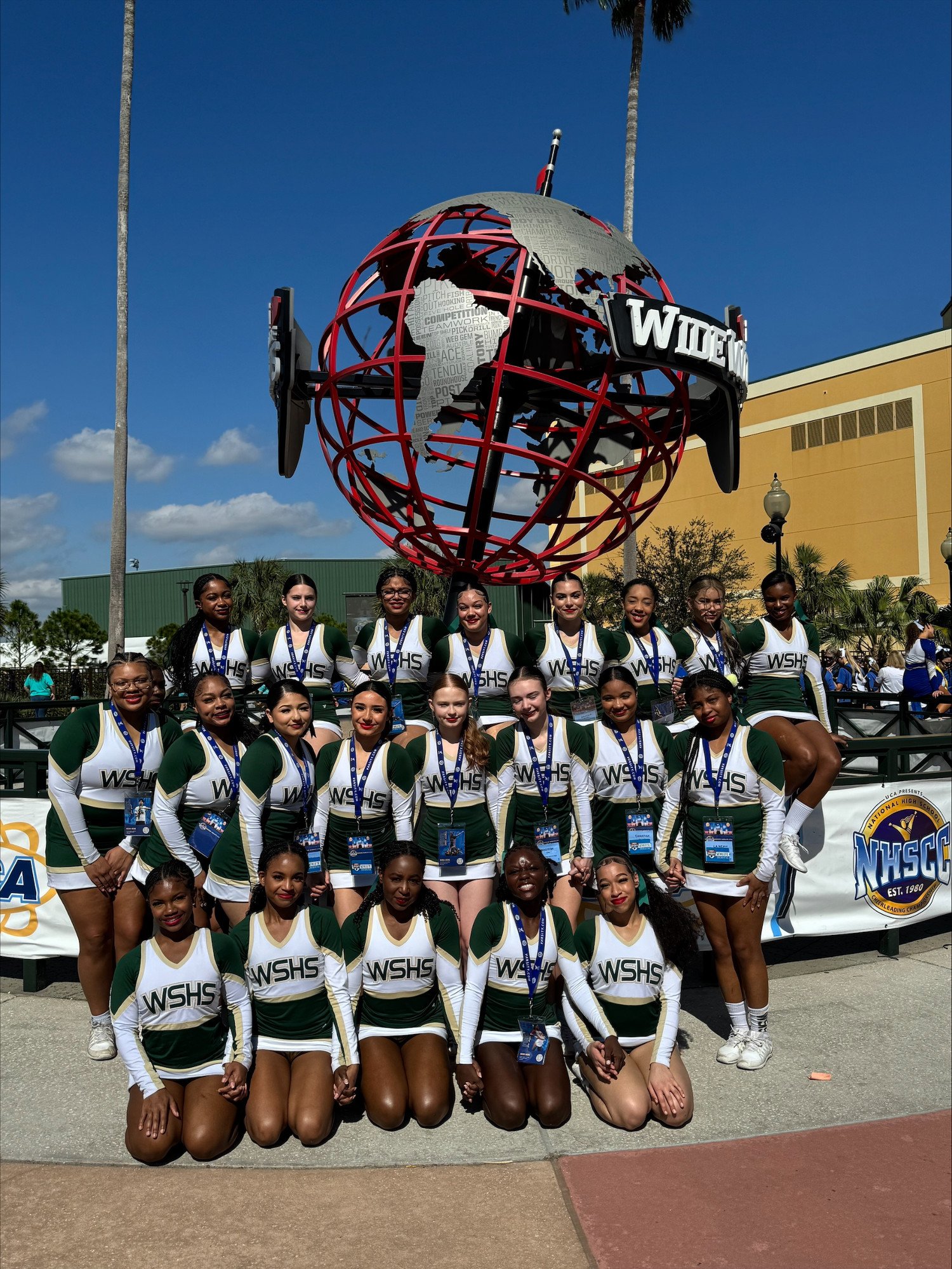 Group photo of the WSHS cheerleading team in front of a large globe sculpture at a cheer competition.