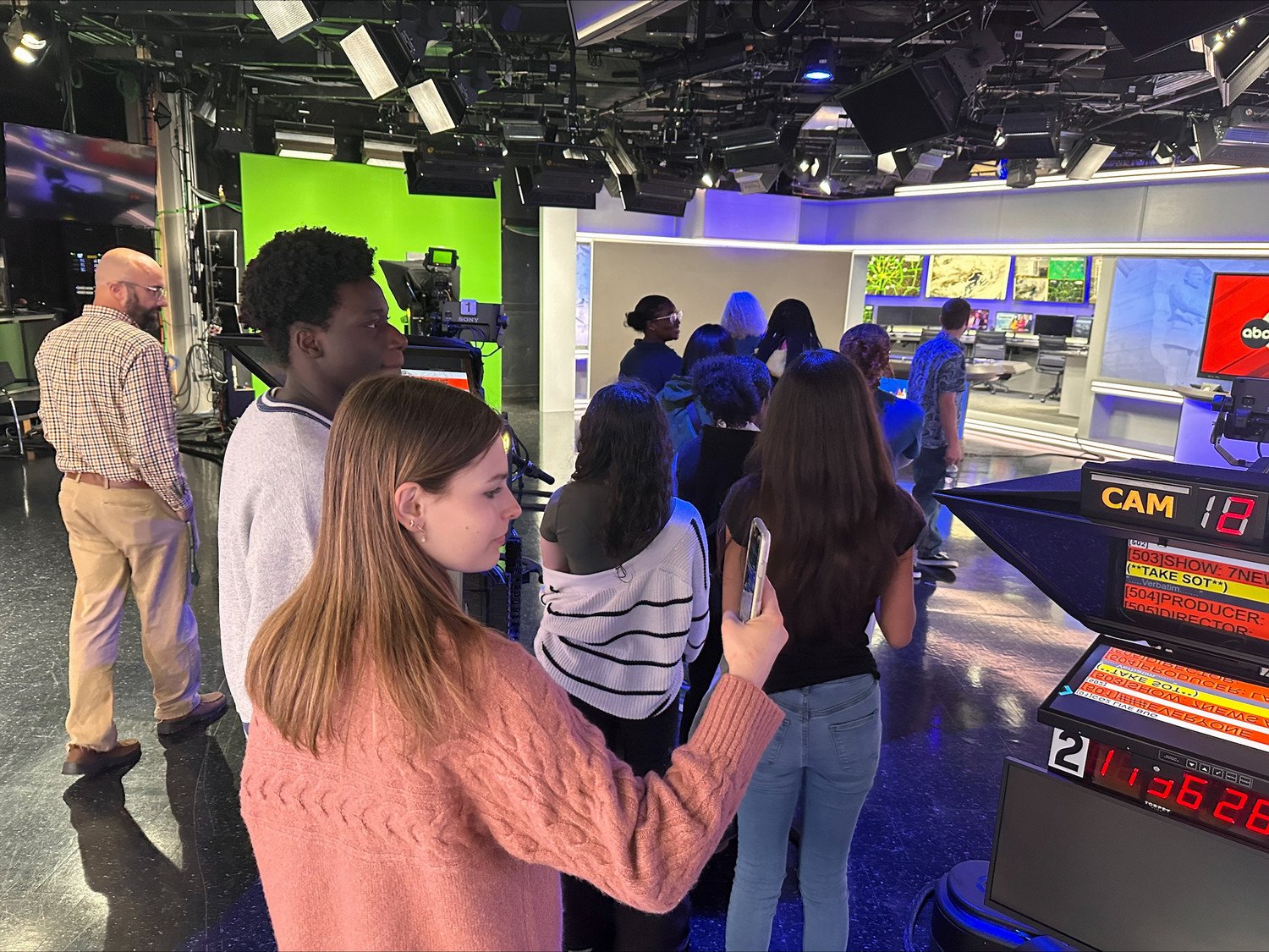 Students on a studio tour at a television station, observing the broadcasting equipment and set.