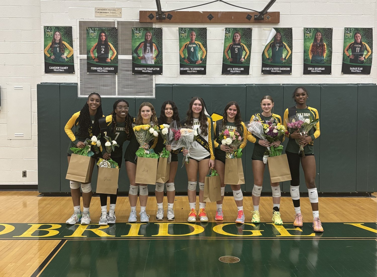 WSHS senior volleyball players recognized on senior night in the gym in front of their senior images on the gym wall. 