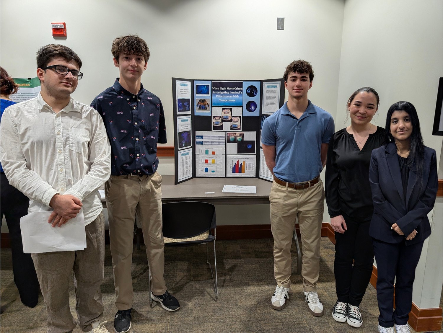 WSHS Students presenting their research project at an academic event, standing next to a display board with charts and images.
